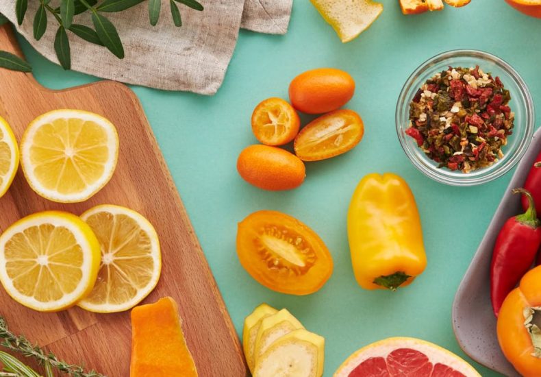 Colorful assortment of sliced fruits and vegetables on teal background, showcasing freshness.