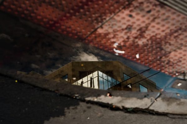 Reflection of a modern architectural building in a sidewalk puddle with textured surfaces.