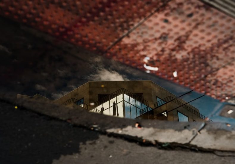 Reflection of a modern architectural building in a sidewalk puddle with textured surfaces.